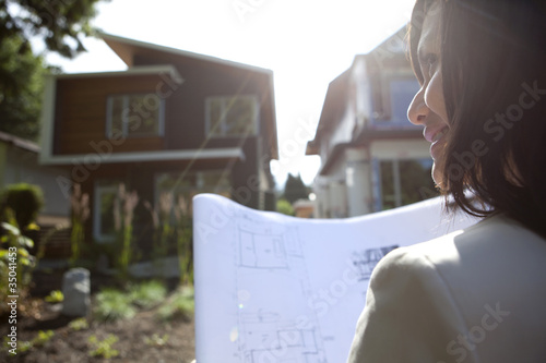 Mixed race real estate agent standing near house reviewing blueprints photo