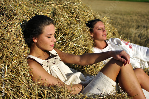 two girls in traditional Russian costume resting on a haystack