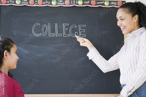 Girl watching teacher write the word “college” on blackboard photo