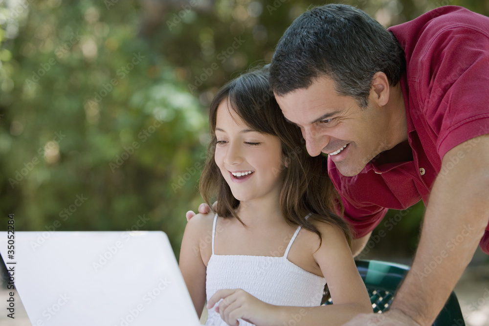 Hispanic father watching daughter use laptop Hispanic father watching daughter use laptop