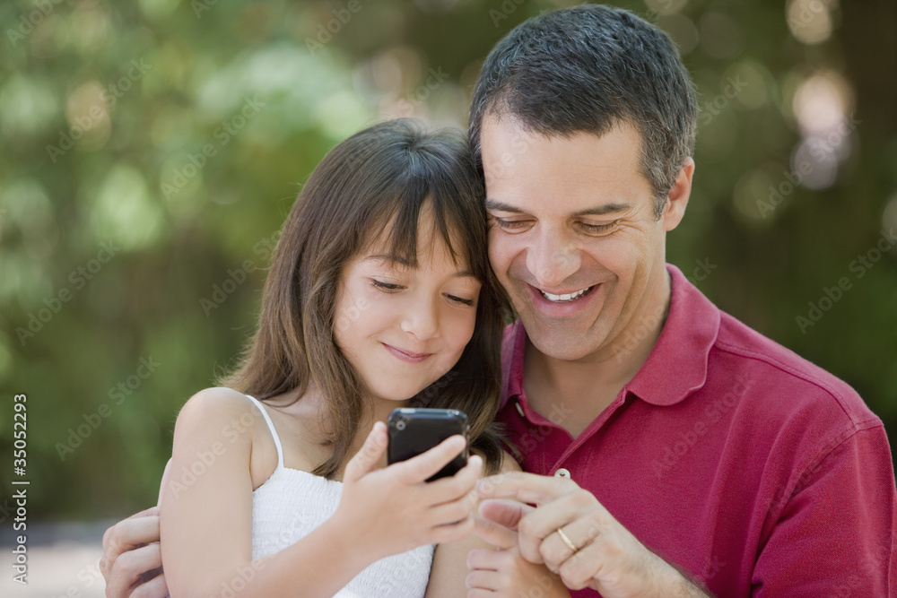 Hispanic father and daughter text messaging on cell phone Hispanic father and daughter text messaging on cell phone