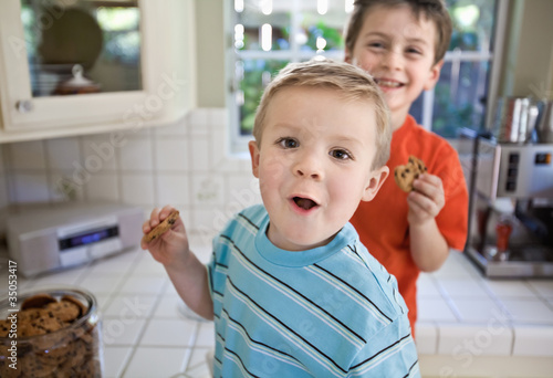 Caucasian brothers sneaking cookies in kitchen
