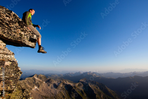 Young man sitting on rock above mountain range