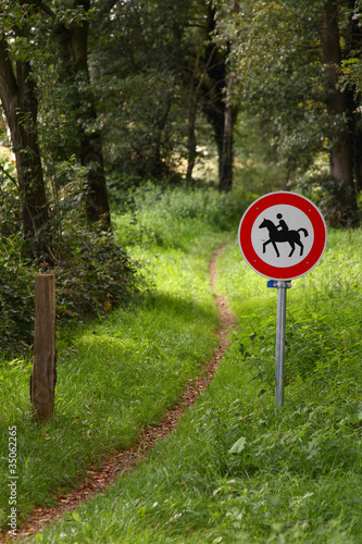 Verbotschild für Reiter vor einem idyllischen Wanderweg