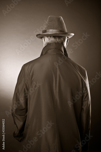 The man in a raincoat and a hat. The rear view