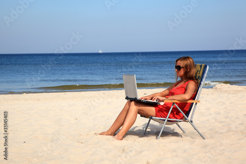 Young woman with laptop is sitting on the sunny beach. © Piotr Pawinski