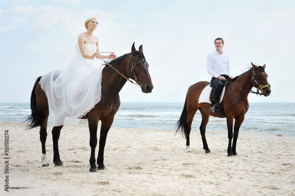 Fototapeta premium Beach wedding: bride and groom on a horses by the sea
