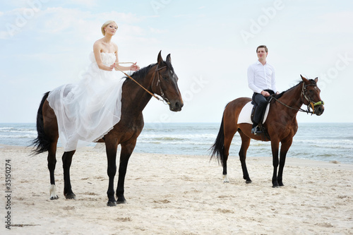 Fototapeta Naklejka Na Ścianę i Meble -  Beach wedding: bride and groom on a horses by the sea