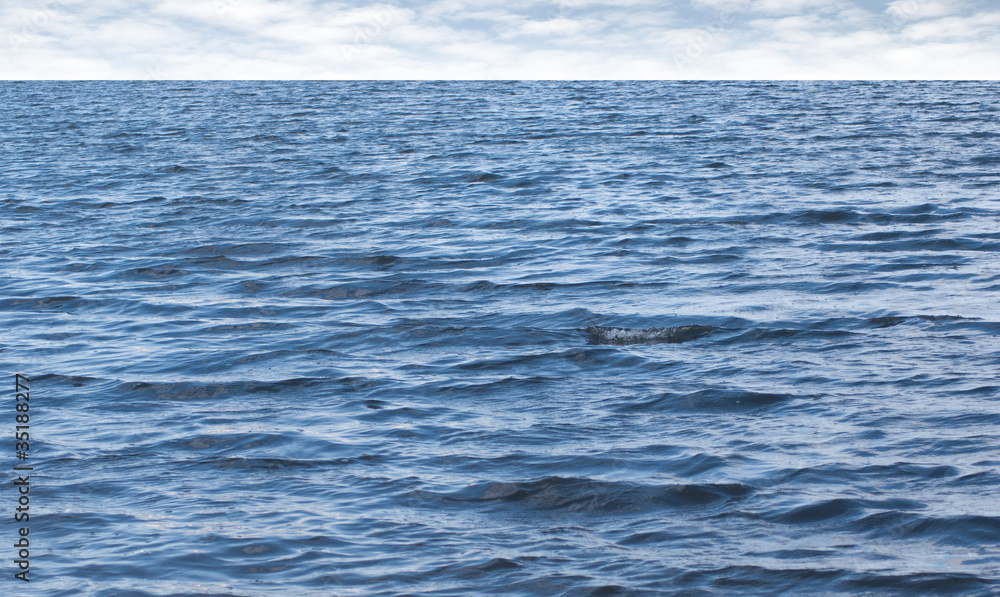 Small waves on pure blue sea water with cloudy sky on horizon Small waves on pure blue sea water with cloudy sky on horizon