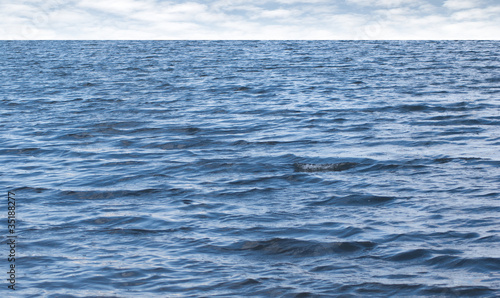 Small waves on pure blue sea water with cloudy sky on horizon
