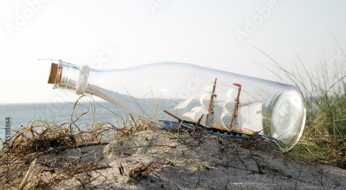Miniature ship in bottle standing on sand