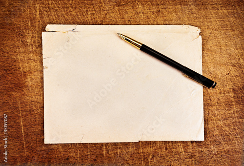 Ink pen and an old torn envelope on a wooden background.