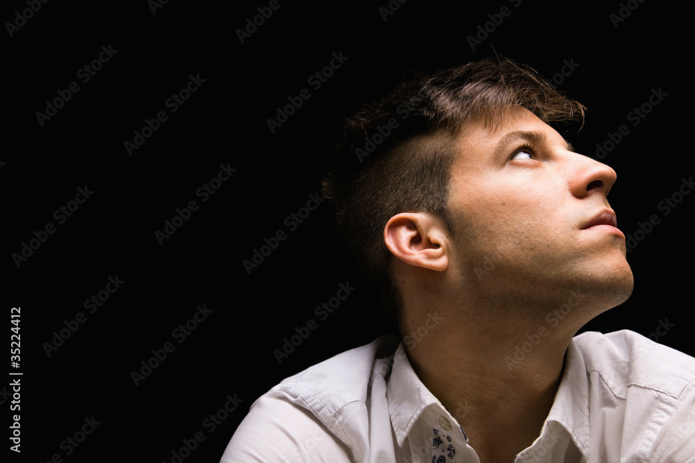 Portrait of a young man looking up against black background Portrait of a young man looking up against black background