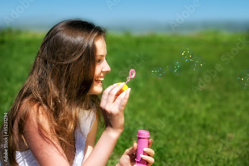Young girl blowing soap bubbles in summer green park