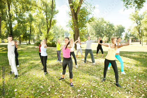 group of people exercising yoga in park © luckybusiness