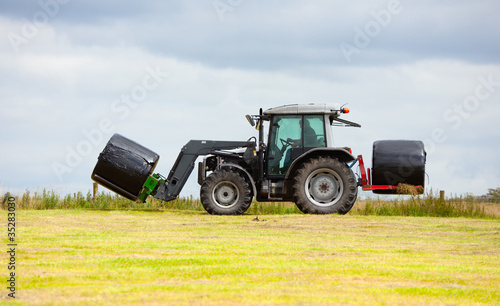 tractor collecting a roll of haystack in the field