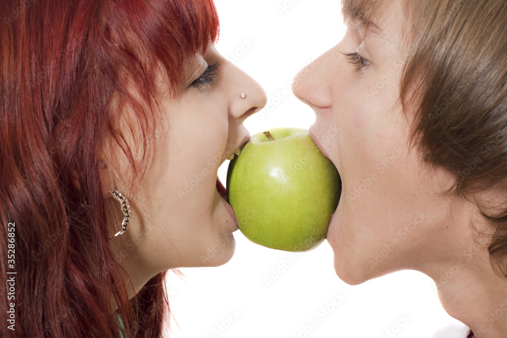 Close-up of happy couple biting a green apple from another sides Close-up of happy couple biting a green apple from another sides