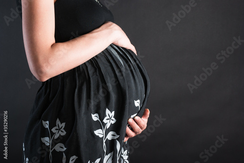 Stomach of the pregnant woman in a dark dress with white colors