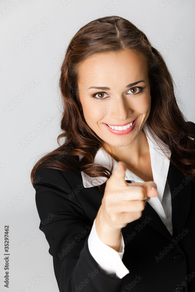Business woman pointing finger at viewer, over grey Business woman pointing finger at viewer, over grey