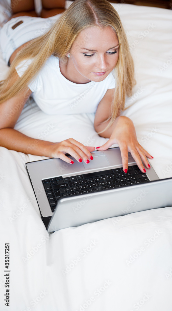 Smiling woman using a laptop while lying on her bed Smiling woman using a laptop while lying on her bed