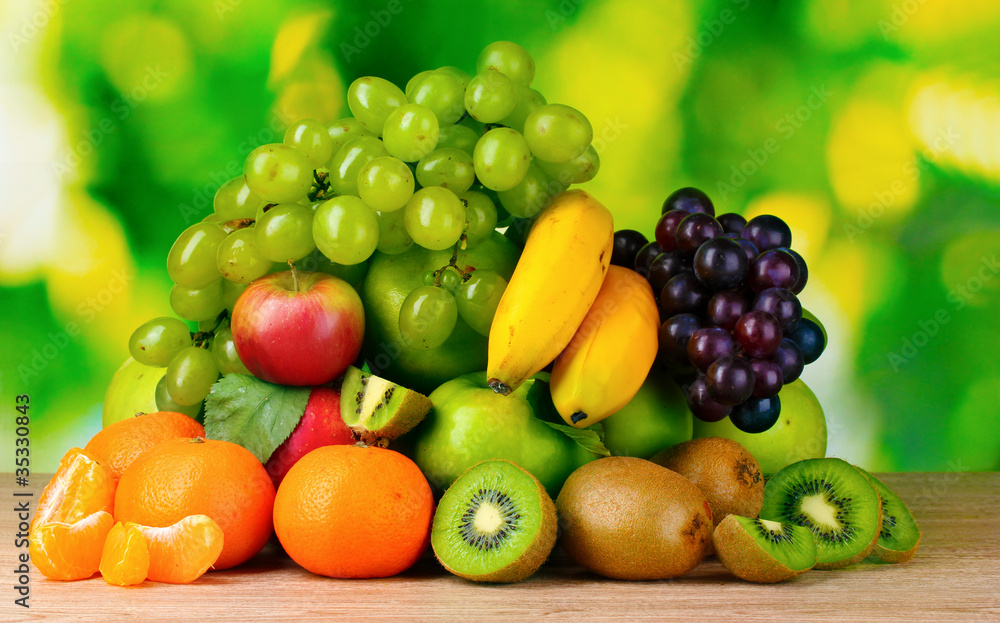 Ripe juicy fruits on wooden table on green background