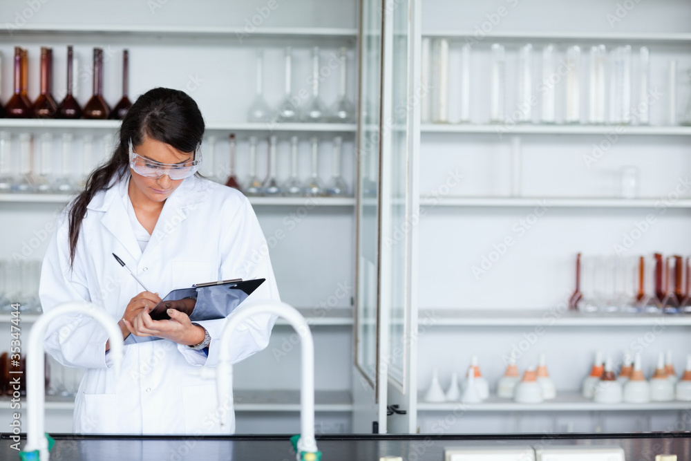 Focused female scientist writing on a clipboard Focused female scientist writing on a clipboard