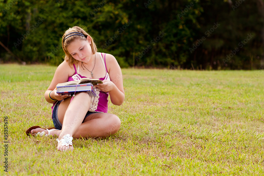 Fototapeta premium Teenage girl studying for school outdoors on field