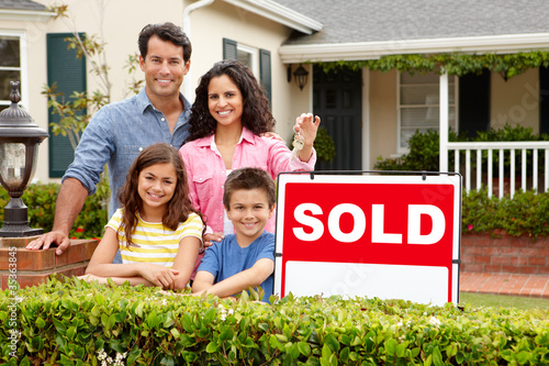 Hispanic family outside home with sold sign photo