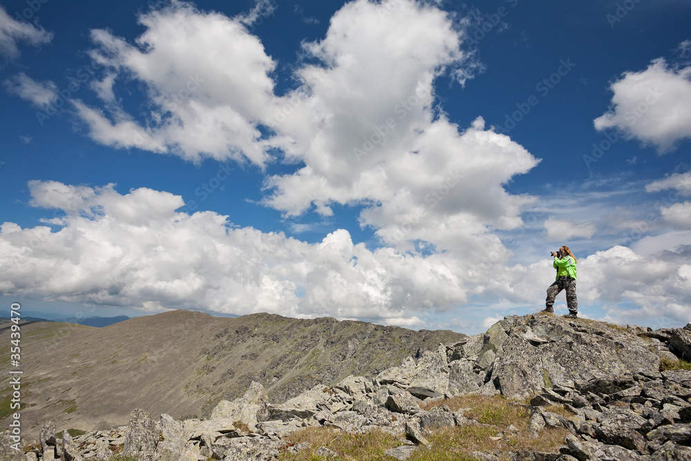 girl-tourist photographs in mountains, standing on a rock.