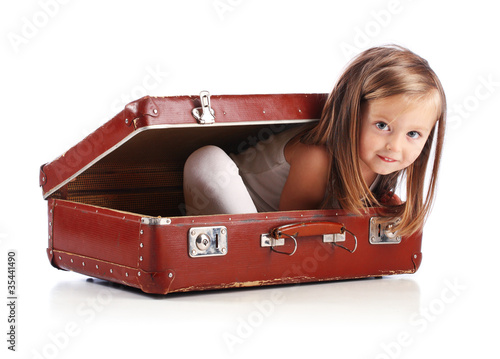 Happy small girl sitting in a suitcase. Travel concept. Isolated