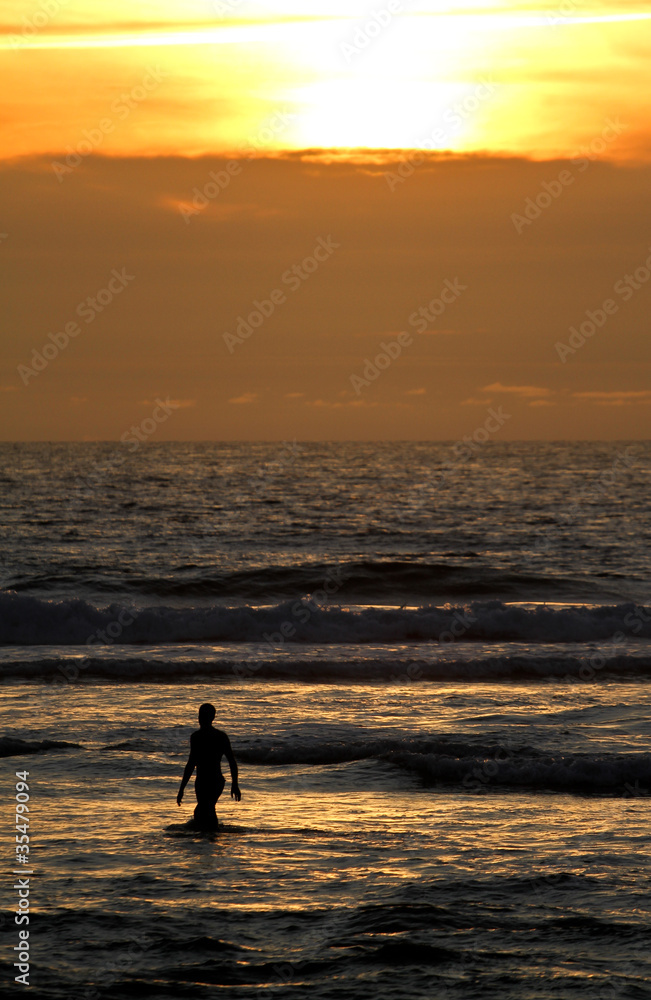 silhouette of man walking in ocean in sunset
