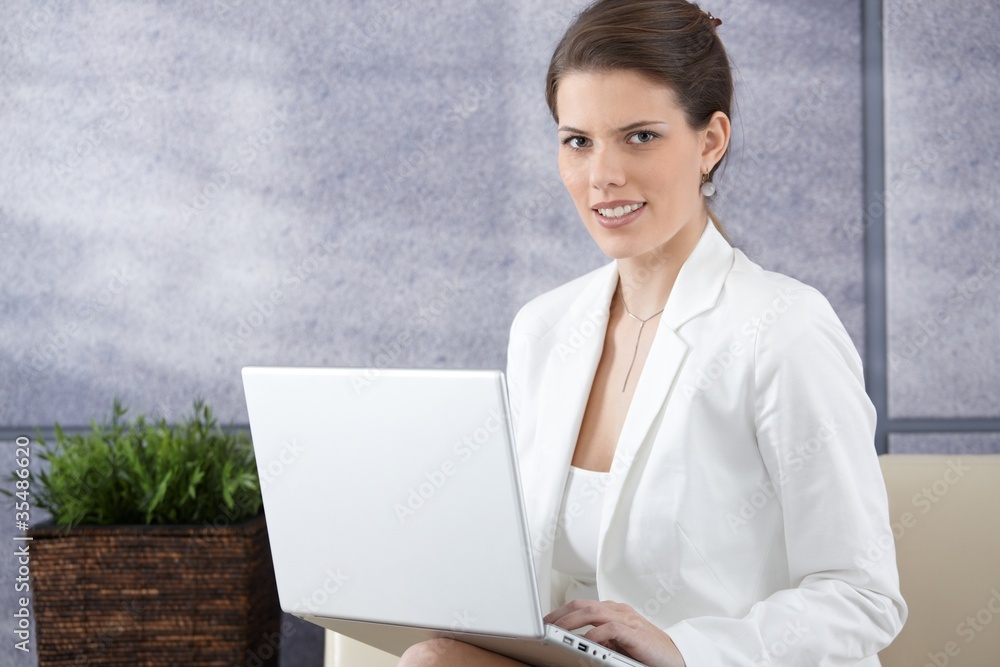 Smiling young businesswoman on sofa with computer Smiling young businesswoman on sofa with computer