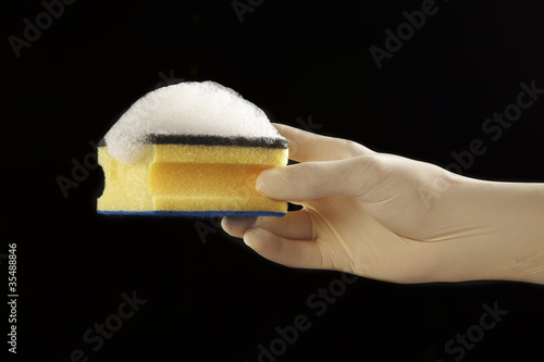 mano con guante de latex con esponja con jabón en fondo negro photo