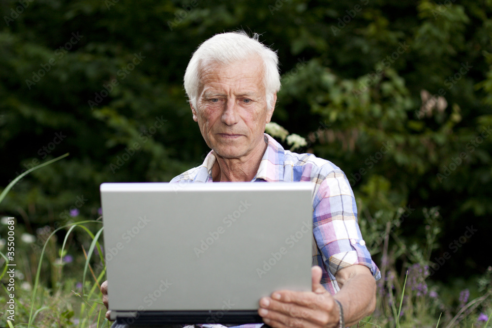 An elderly man sits in the woods with a laptop An elderly man sits in the woods with a laptop
