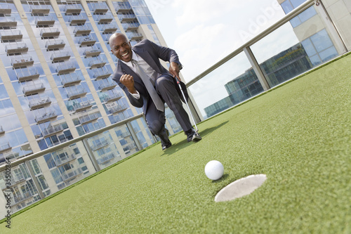 African American Businessman Playing Golf on Skyscraper Rooftop photo