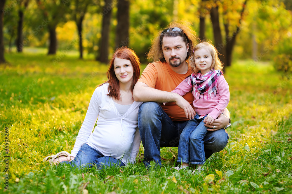 Fototapeta premium Beautiful expecting family in autumn park at sunset