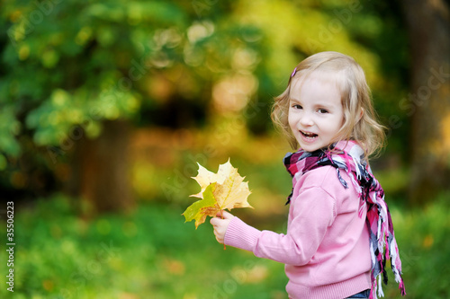 Little girl at autumn park holding yellow leaves