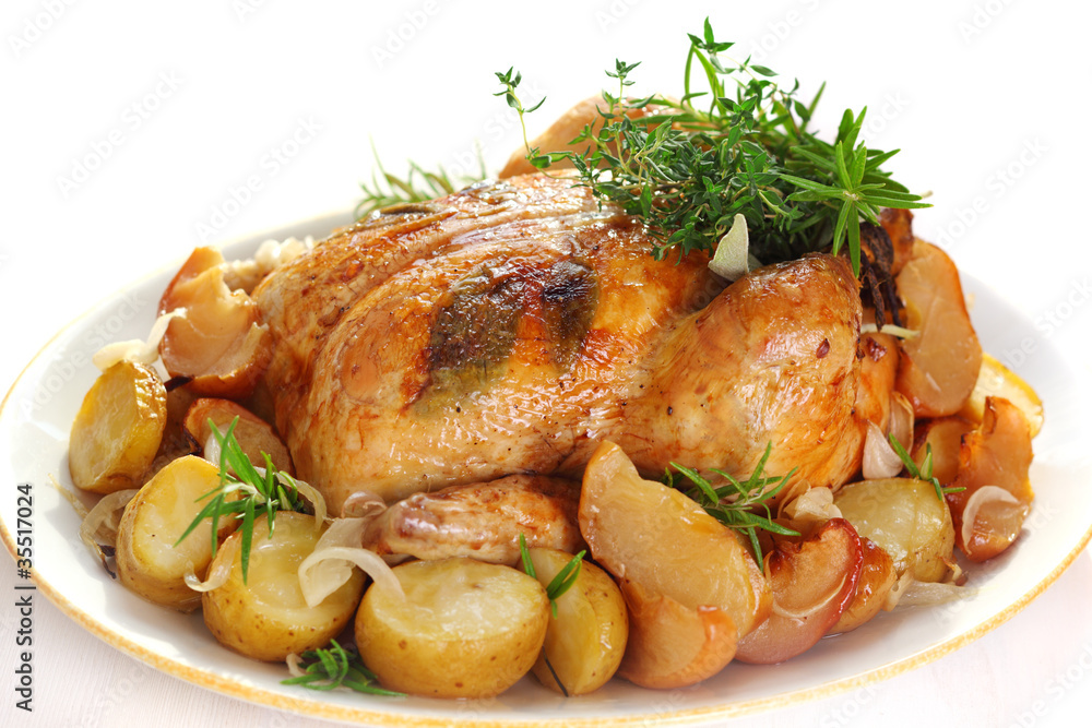 Whole roasted chicken with potatoes and herbs on white plate Whole roasted chicken with potatoes and herbs on white plate