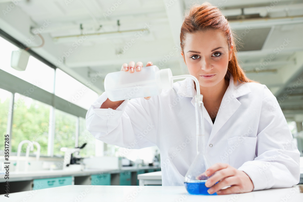 Red-haired scientist pouring liquid in a flask Red-haired scientist pouring liquid in a flask