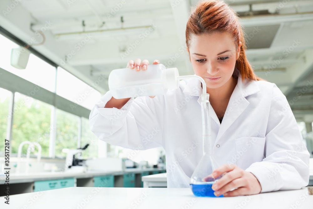 Red-haired focused scientist pouring liquid in a flask Red-haired focused scientist pouring liquid in a flask