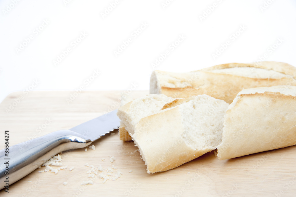 Baguette and bread knife on chopping board isolated on white