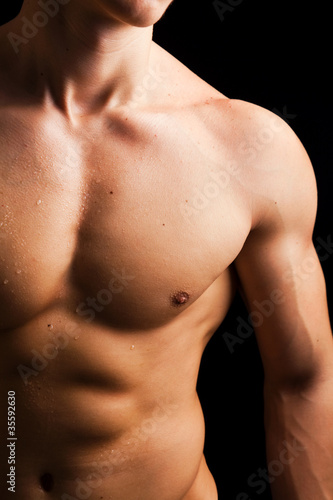 Young man with naked muscled torso against black background