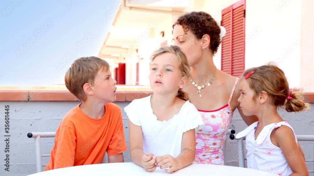 Woman and three kids are sitting at table and talking Woman and three kids are sitting at table and talking