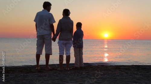 Parents and son standing on beach holding hands photo