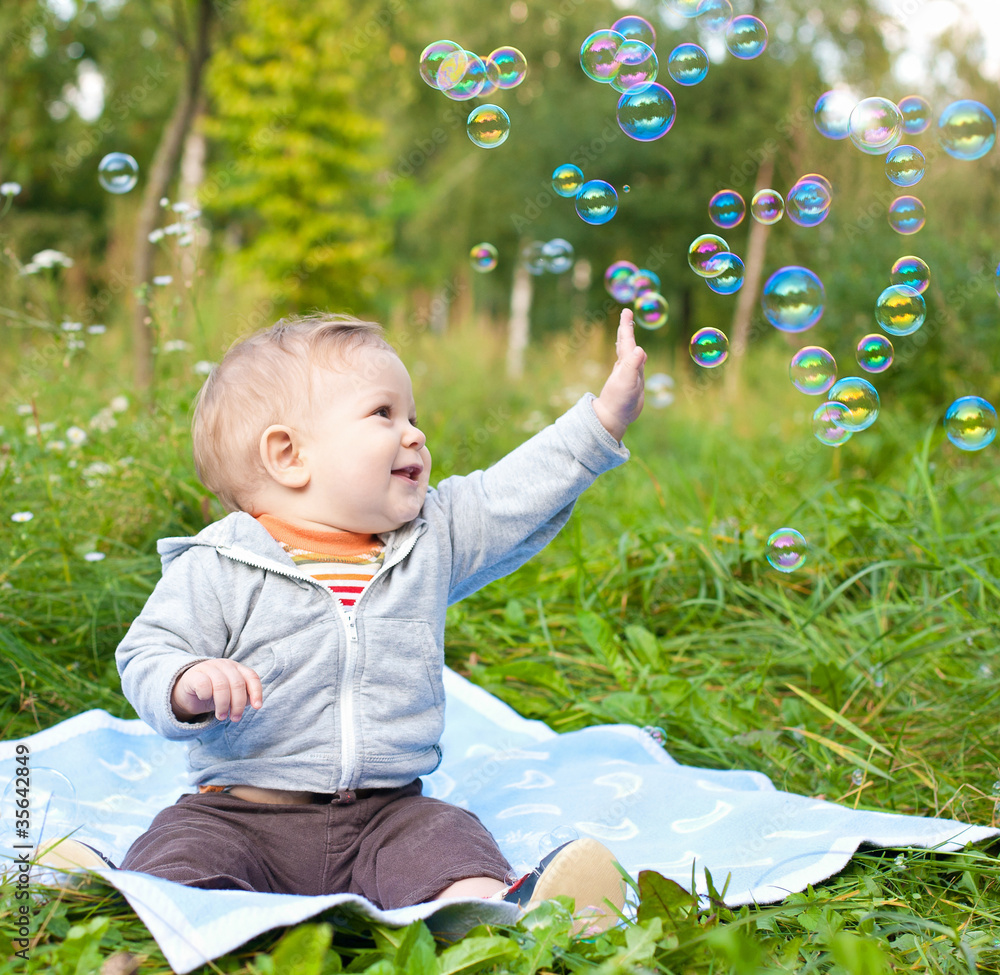 boy sitting on green grass outdor playing with soap bubbles boy sitting on green grass outdor playing with soap bubbles