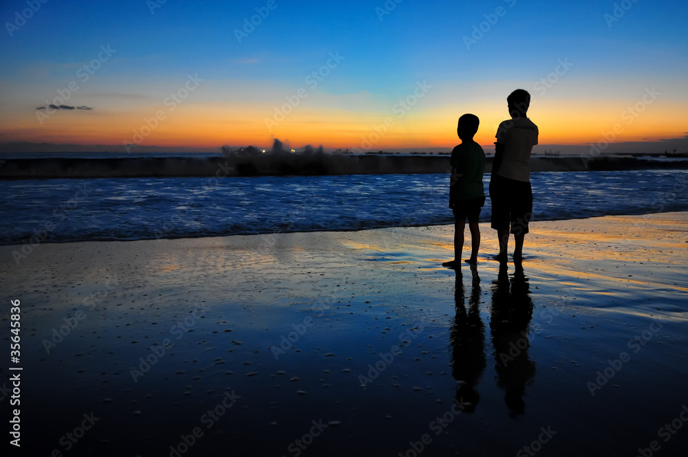 Two boys at ocean coast at sunset