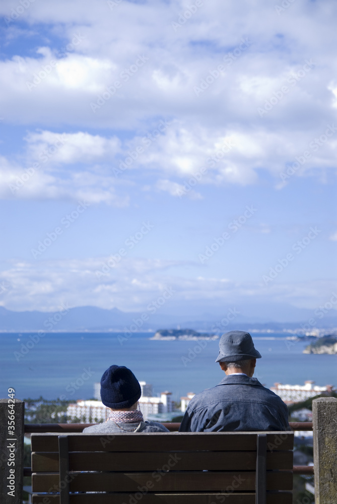 公園のベンチで海を見つめるシニアの夫婦