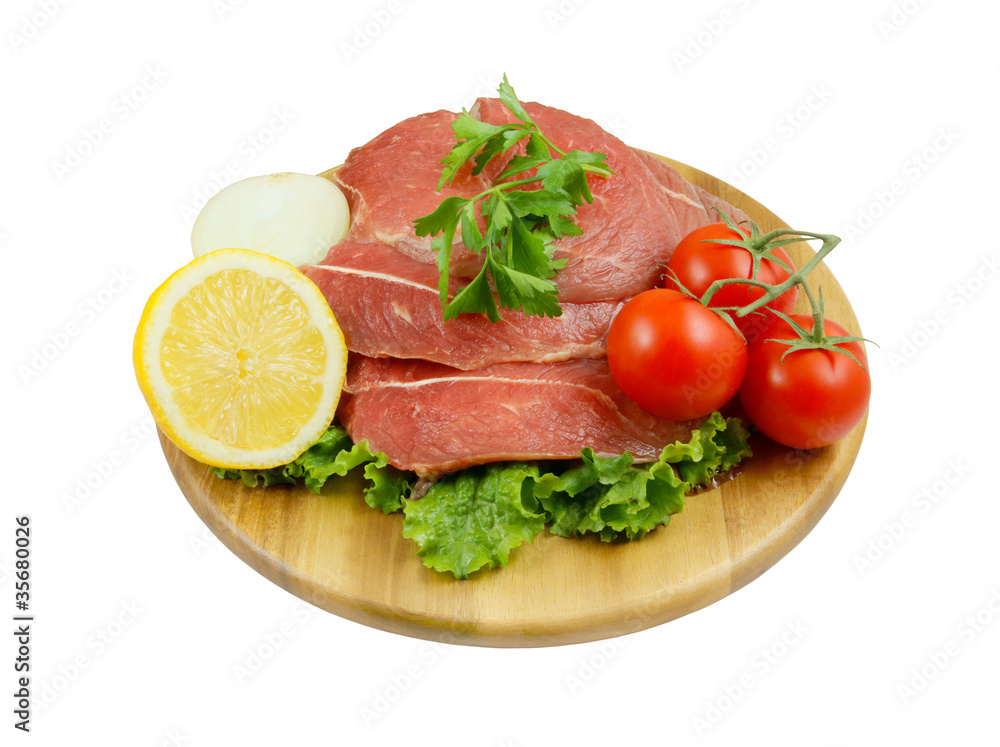 Raw beef meat with lemon, tomato and greens on cutting board