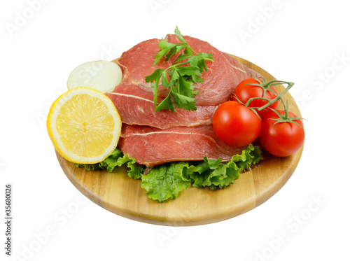 Raw beef meat with lemon  tomato and greens on cutting board