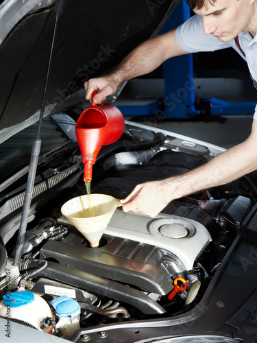 Motor mechanic topping up oil of a car in a garage